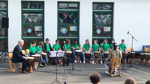 Staatssekretär Lösel sitzt mit Schülerinnen und Schülern im Kreis, alle haben Trommeln und andere INstrumente vor sich stehen.