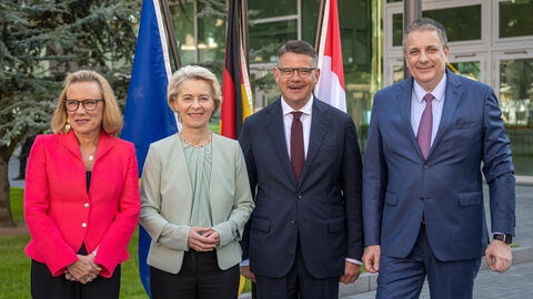 Ministerpräsident Rhein neben Ursula von der Leyen, Belén Garijo und Kai Beckmann. Sie stehen nebeneinander vor Flaggen.