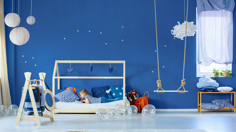 Mädchen liegt im Zimmer auf dem Bett und liest. Die Wand ist dunkelblau mit Sternen.