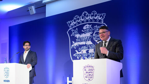 Boris Rhein steht an einem Rednerpult - im Hintergrund sieht man das neue Logo. 