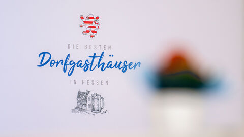 Nahaufnahme von einem weißen Aufsteller. Darauf steht geschrieben "Die Besten Dorfgasthäuser in Hessen".